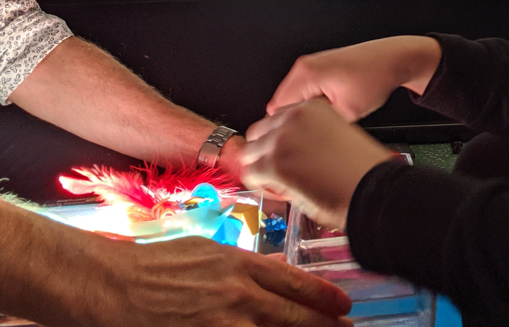 An adult and a child are exploring different items in a sensory bin. Hands of an adult and a child working through different items in a sensory bin